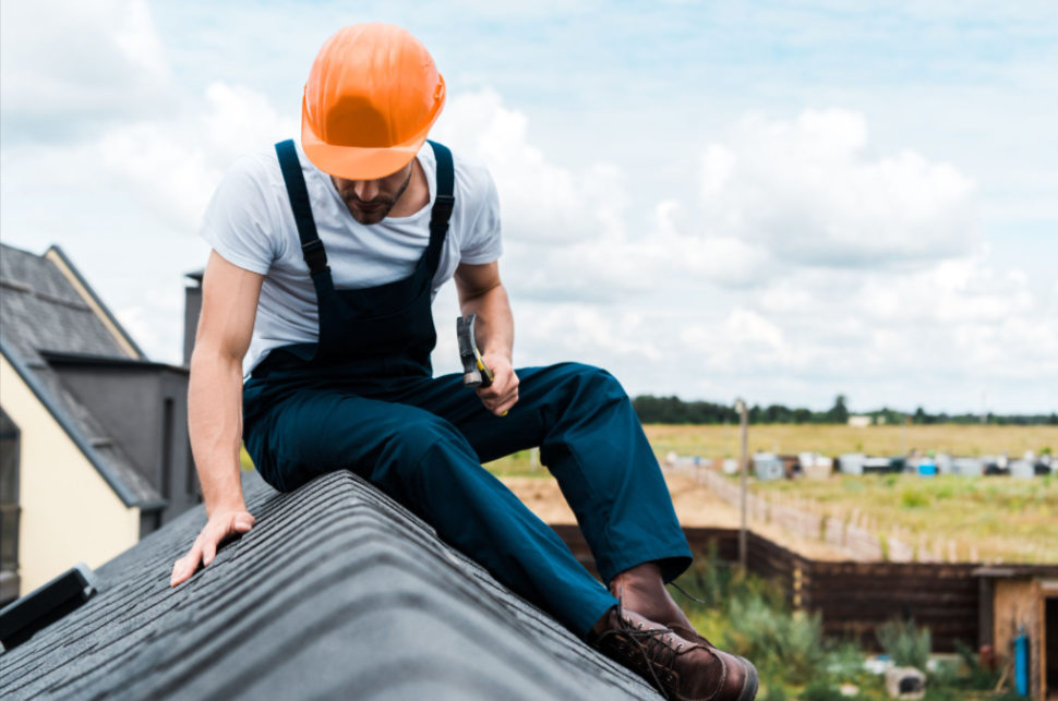 Roofer wearing an orange safety helmet using a hammer to inspect and assess the condition of a home’s roof