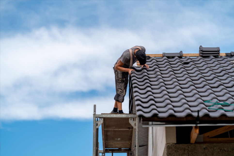 Roofing professional on scaffolding, placing ceramic tiles during roof installation