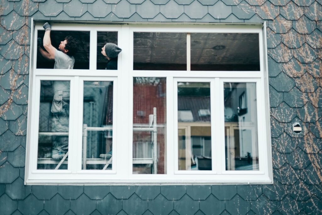 Two men secure a plastic window frame during a house window replacement