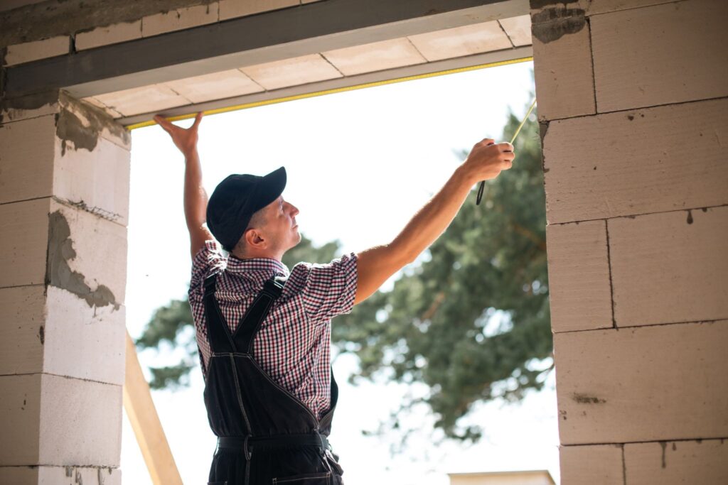 An installer measuring the width of the garage door opening next to the brick wall during a home improvement project