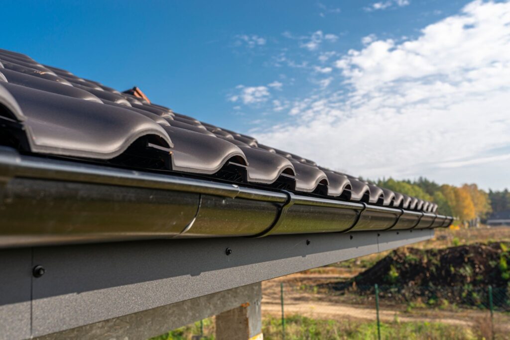 Close-up view of a black metal gutter attached to a ceramic tile roof