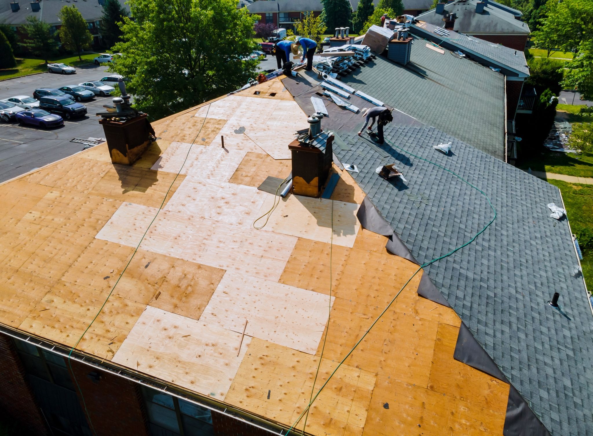 Roof replacement with new asphalt shingles on an apartment building, with workers installing materials across a multi-unit residential roof