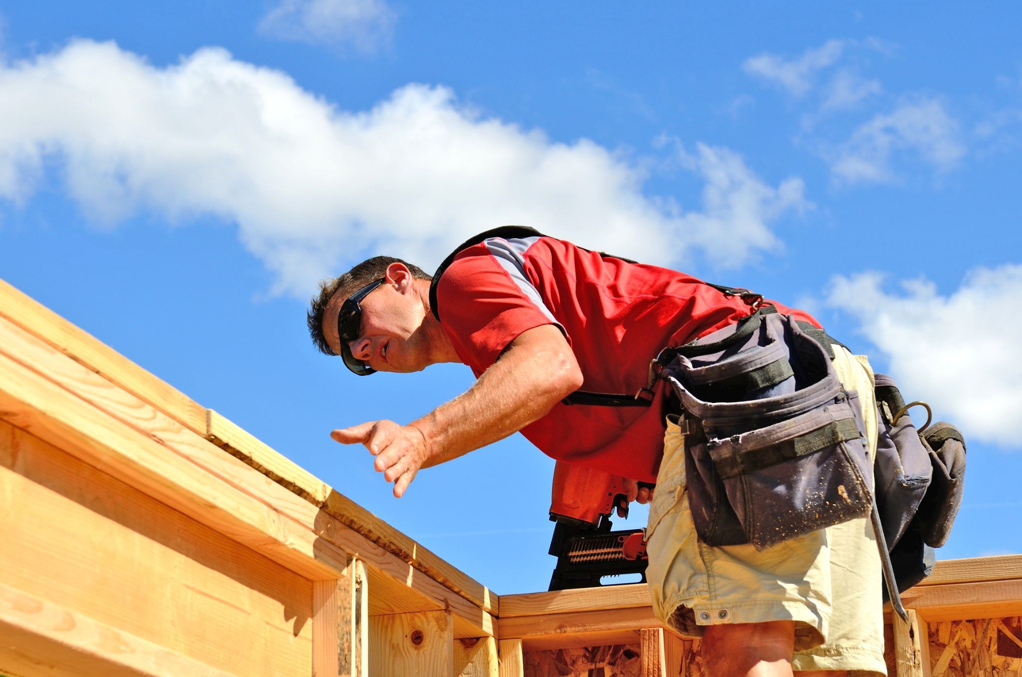 Roofing professional with a pneumatic nailer inspects the materials along the corner of the roof