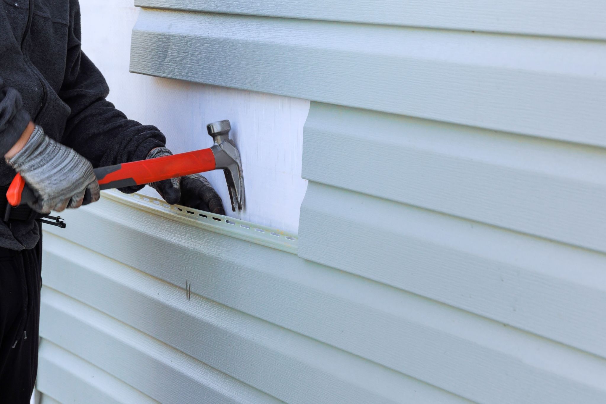 A contractor removing damaged home siding with a hammer to inspect the underlying structure and assess repair needs