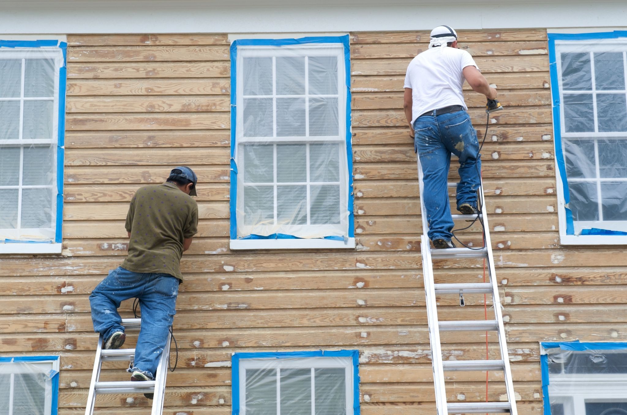 Two workers installing replacement siding on a residential home using ladders